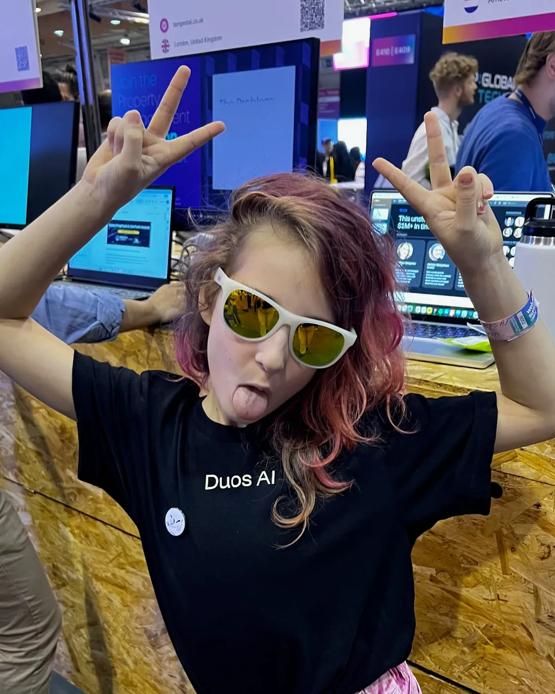 One of the crew at the Duos stand at Web Summit, in white sunglasses and a Duos AI T-shirt, tongue out, making peace signs