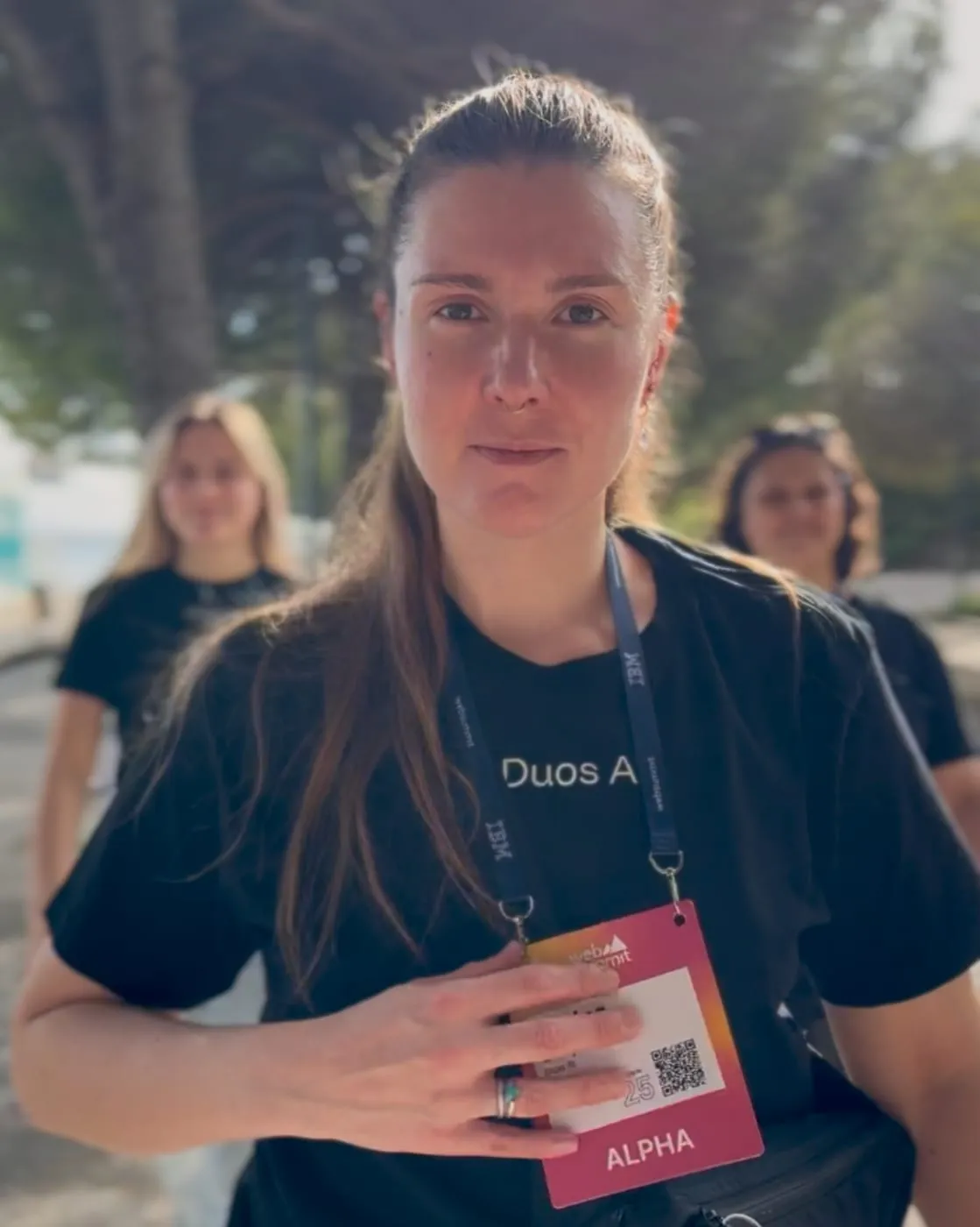 One of the crew walking straight at the camera in a Duos AI T-shirt and a Web Summit ALPHA badge, hand on her chest, looking determined, two more of the crew a few steps behind
