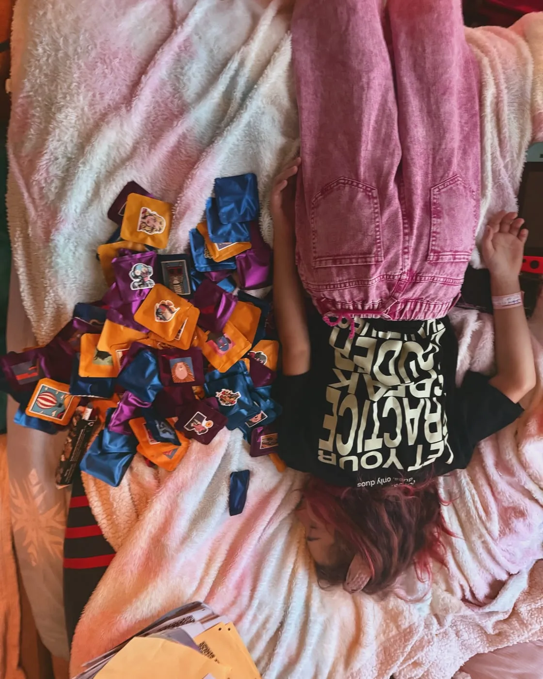 Seen from above: a heap of Duos mystery boxes on a bed, and one of the crew lying flat out beside them